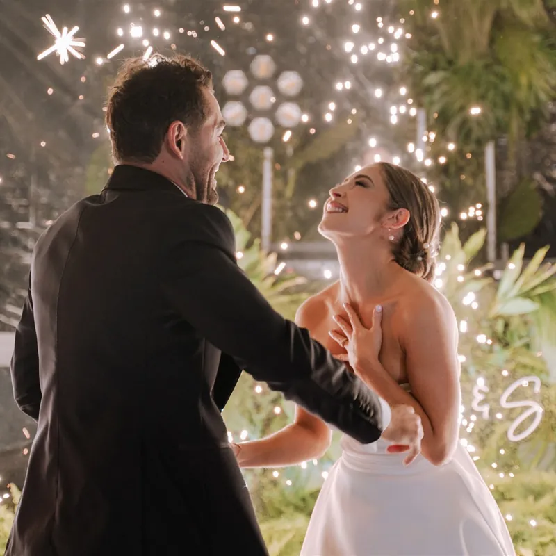Novios bailando de noche entre luces y flores