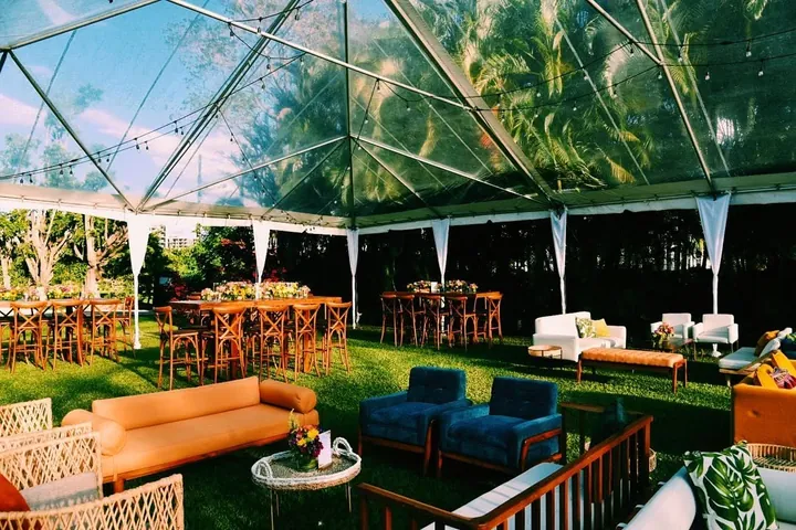 Salas y mesas de madera bajo la carpa transparente, rodeadas de jardín