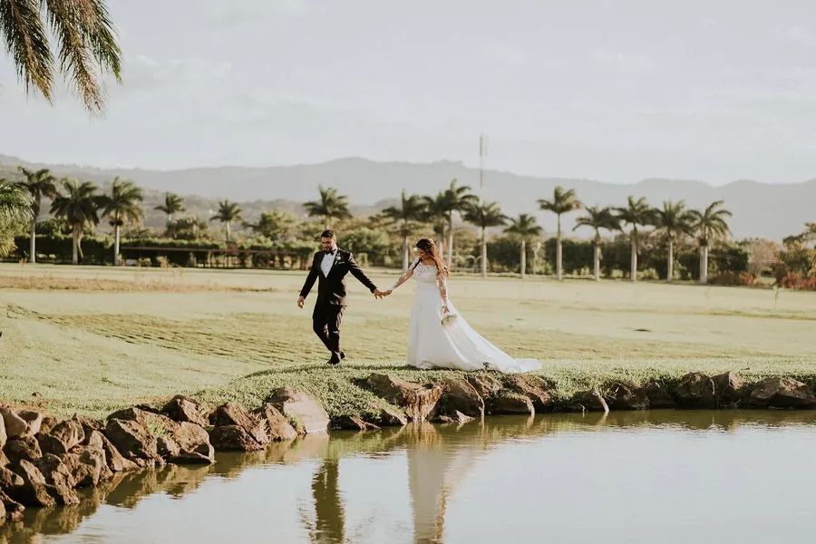 Novios caminando junto a la laguna, con palmeras y montañas al fondo